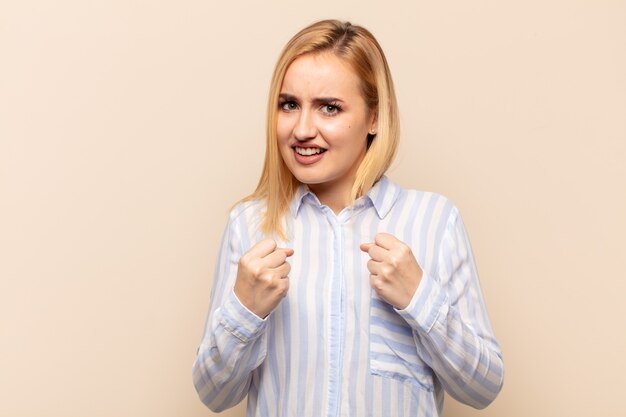 Jeune femme blonde à la confiance, en colère, forte et agressive, avec les poings prêts à se battre en position de boxe