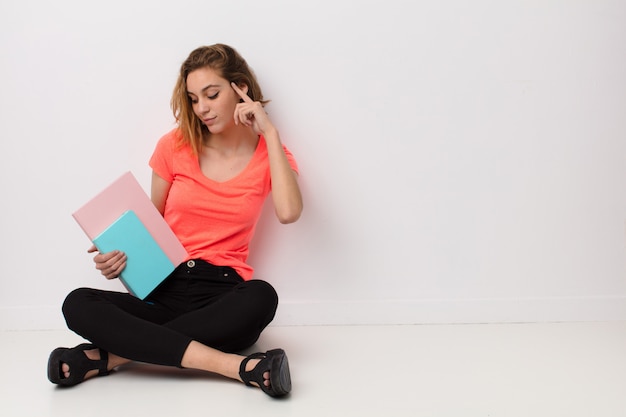 Jeune femme blonde contre un mur de couleur plat avec des livres