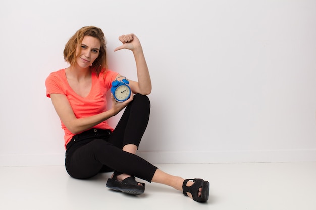 Jeune femme blonde contre le mur avec un réveil