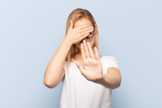 Jeune femme blonde couvrant le visage avec la main et mettant l'autre main à l'avant pour arrêter la caméra, refusant des photos ou des images