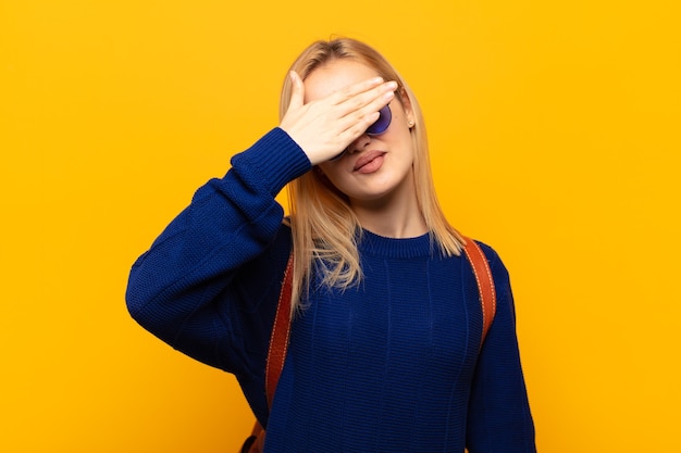 Jeune femme blonde couvrant les yeux d'une main se sentant effrayé ou anxieux, se demandant ou attendant aveuglément une surprise