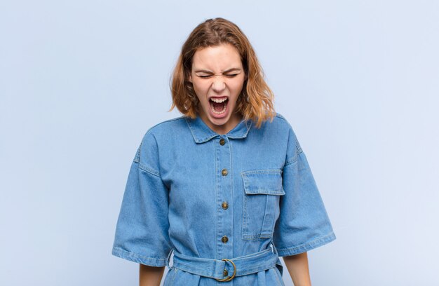 Jeune femme blonde criant agressivement, l'air très en colère, frustré, outré ou ennuyé, ne criant pas contre le mur de couleur plat