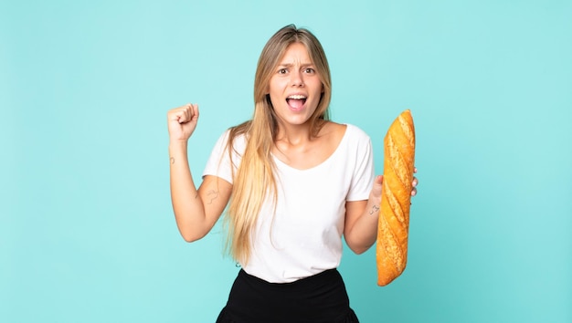 Jeune femme blonde criant agressivement avec une expression de colère et tenant une baguette de pain