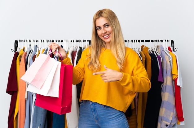 Jeune femme blonde dans un magasin de vêtements et tenant des sacs à provisions et en le pointant