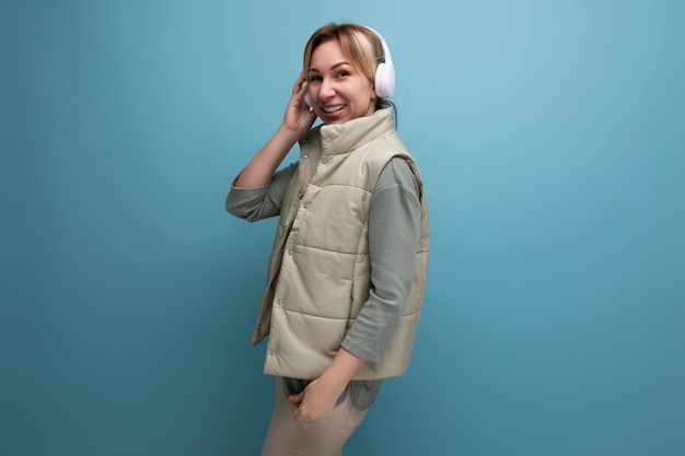 Jeune femme blonde dans un style décontracté avec un casque sans fil sur un fond bleu isolé avec