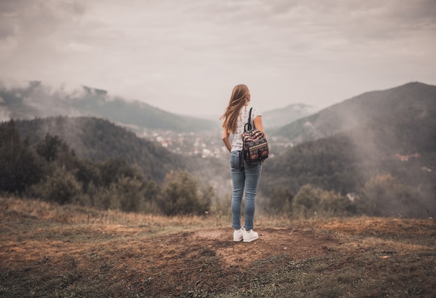 Jeune femme blonde debout seule avec sac à dos sur les montagnes de la forêt sauvage