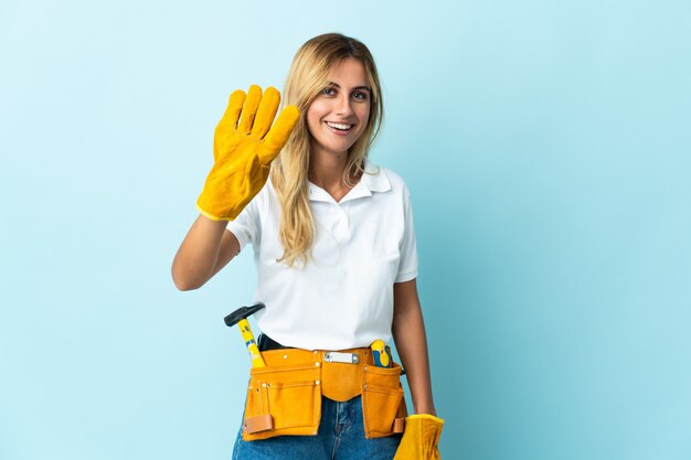 Jeune femme blonde électricien uruguayen isolé sur mur bleu heureux et comptant quatre avec les doigts