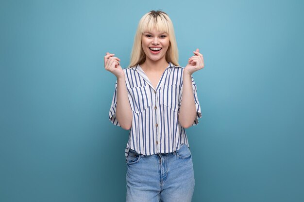 Jeune femme blonde énergique positive en tenue décontractée avec smartphone en studio