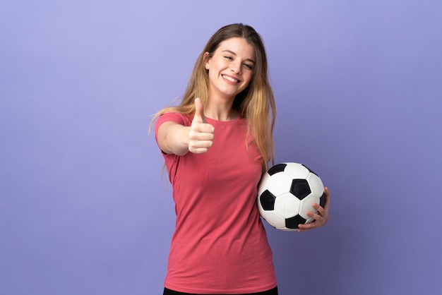 Jeune femme blonde sur un espace isolé avec ballon de foot et avec le pouce vers le haut