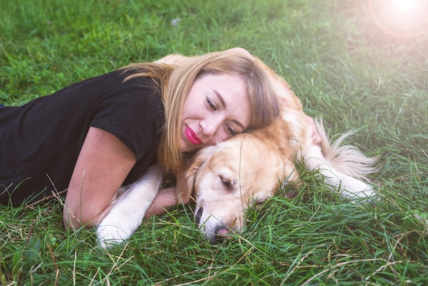 Une jeune femme blonde est allongée sur l'herbe avec son chien. Chien de race retriever avec une fille dans le parc.
