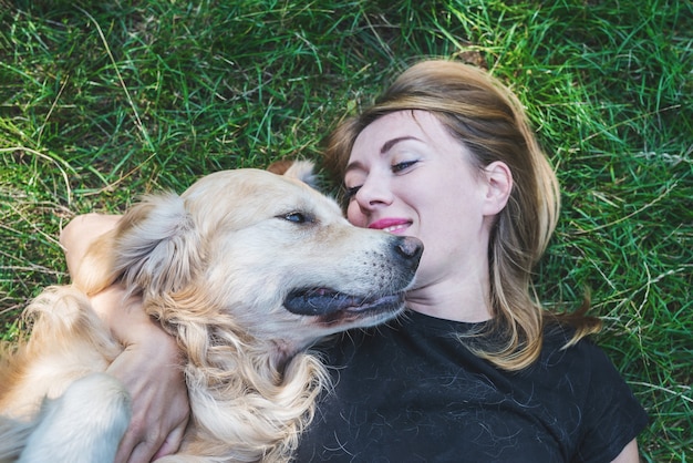 Une jeune femme blonde est allongée sur l'herbe avec son chien. Chien de race retriever avec une fille dans le parc.