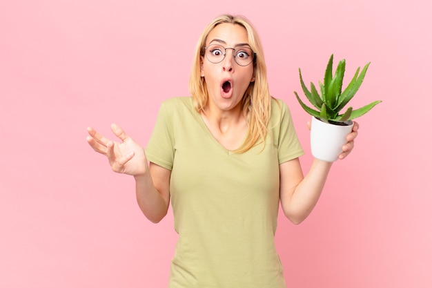 Jeune femme blonde étonnée, choquée et étonnée d'une incroyable surprise et tenant un cactus