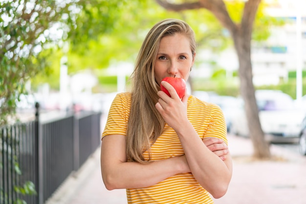 Une jeune femme blonde à l'extérieur mangeant une pomme.