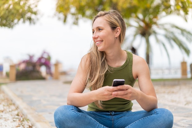 Une jeune femme blonde à l'extérieur en utilisant un téléphone portable