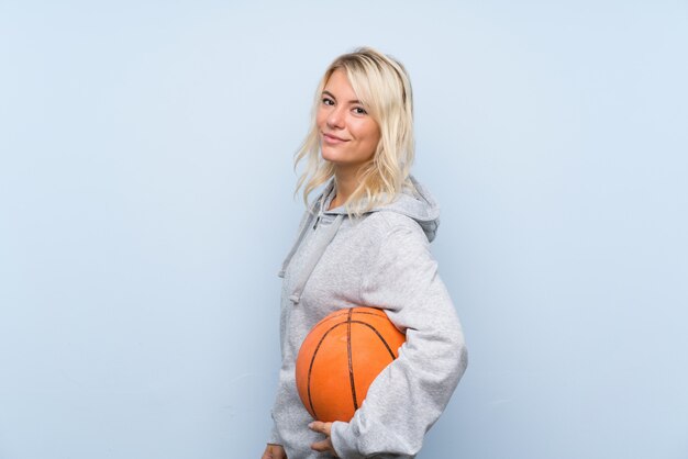 Jeune femme blonde sur fond isolé avec ballon de basket