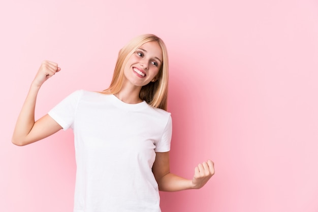 Jeune femme blonde sur fond rose levant le poing après une victoire, concept gagnant.