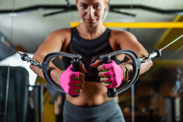 Jeune femme blonde en forme d'exécuter l'exercice avec la machine d'exercice Cable Crossover dans la salle de sport. Concentrez-vous sur les mains