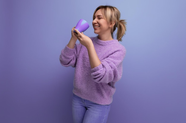 Jeune femme blonde gaie du millénaire dans un look décontracté avec une tasse de café sur un fond lumineux