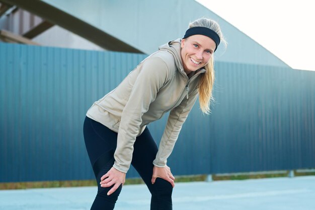 Jeune femme blonde gaie en vêtements de sport regardant la caméra avec le sourire