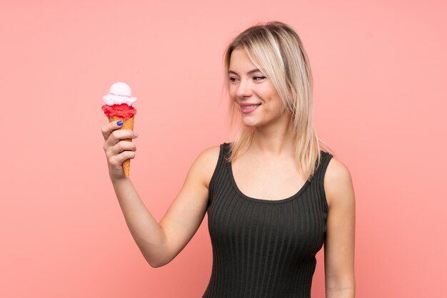 Jeune femme blonde avec une glace au cornet sur un mur rose isolé avec une expression heureuse