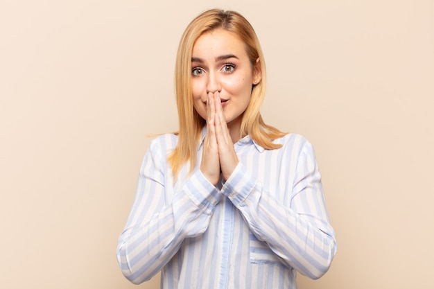 Jeune femme blonde heureuse et excitée, surprise et étonnée couvrant la bouche avec les mains, riant avec une expression mignonne