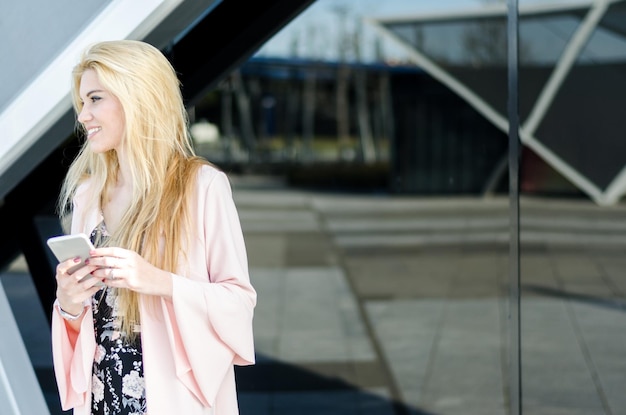 Une jeune femme blonde heureuse à l'extérieur utilisant son téléphone portable isolée