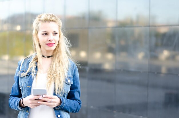 Une jeune femme blonde heureuse à l'extérieur utilisant son téléphone portable isolée