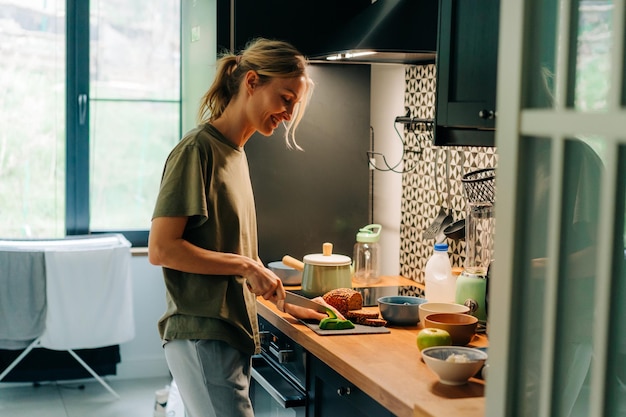 Une jeune femme blonde heureuse souriante cuisinant dans une cuisine domestique