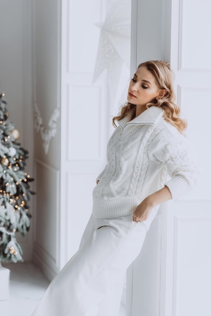 Jeune femme blonde heureuse en vêtements blancs sur le fond d'un sapin de Noël Mise au point sélective douce