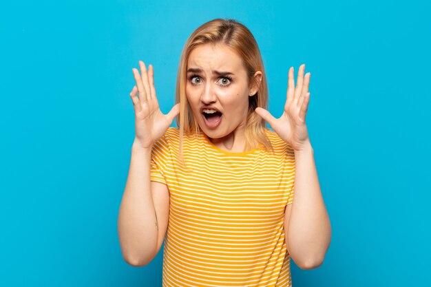 Jeune femme blonde hurlant avec les mains en l'air, se sentant furieuse, frustrée, stressée et bouleversée