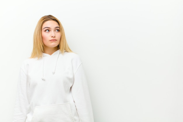 Jeune femme blonde à l'inquiétude, stressé, anxieux et effrayé, paniquant et serrant les dents sur le mur blanc