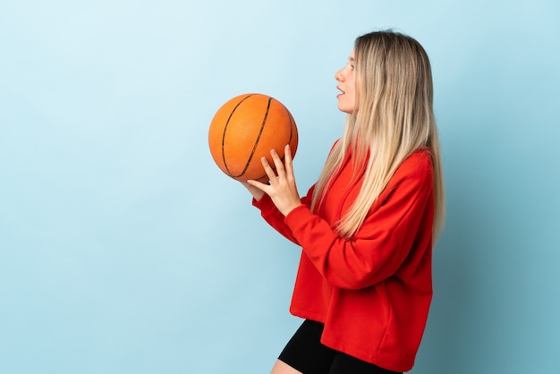 Jeune femme blonde isolée sur bleu jouant au basket