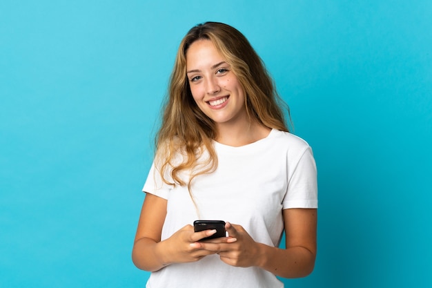 Jeune femme blonde isolée envoyant un message avec le mobile