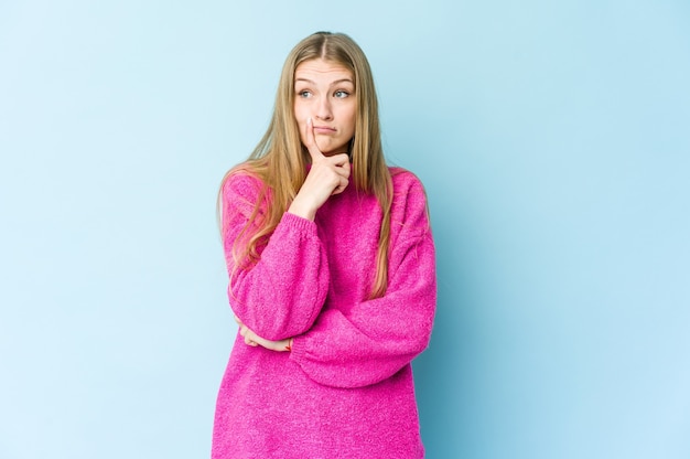 Jeune femme blonde isolée sur fond bleu malheureux à la recherche à huis clos avec une expression sarcastique.