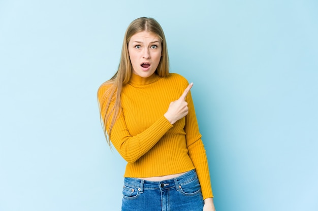 Jeune femme blonde isolée sur fond bleu pointant vers le côté