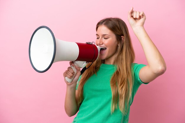 Jeune femme blonde isolée sur fond rose criant à travers un mégaphone pour annoncer quelque chose en position latérale