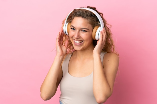 Jeune femme blonde isolée sur fond rose, écouter de la musique