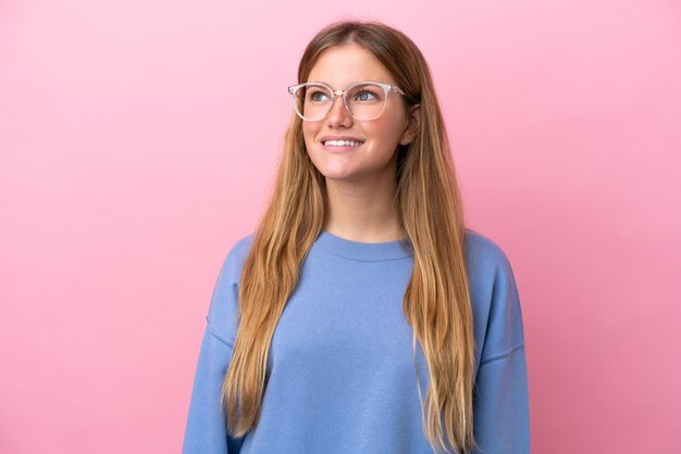 Jeune femme blonde isolée sur fond rose avec des lunettes avec une expression heureuse