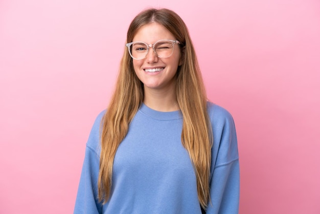 Jeune femme blonde isolée sur fond rose avec des lunettes et une expression heureuse