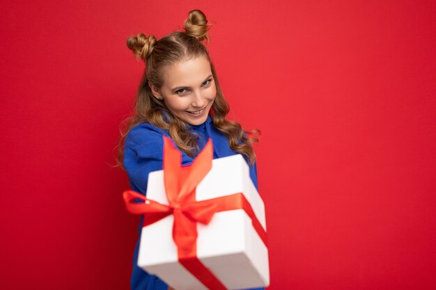 Jeune femme blonde isolée sur fond rouge mur vêtu de bleu tendance