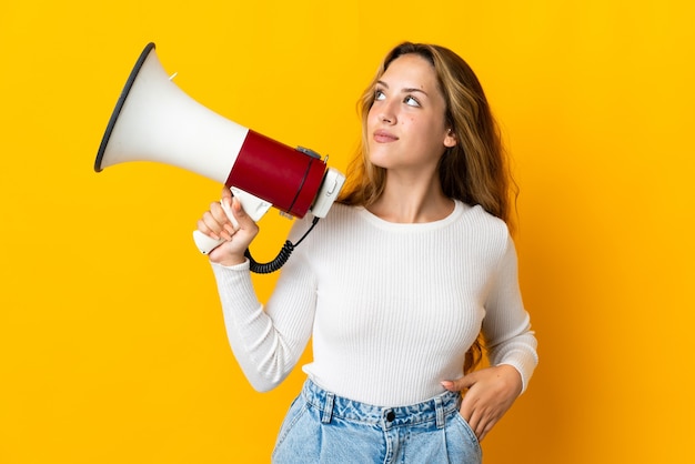 Jeune femme blonde isolée sur jaune tenant un mégaphone pensant