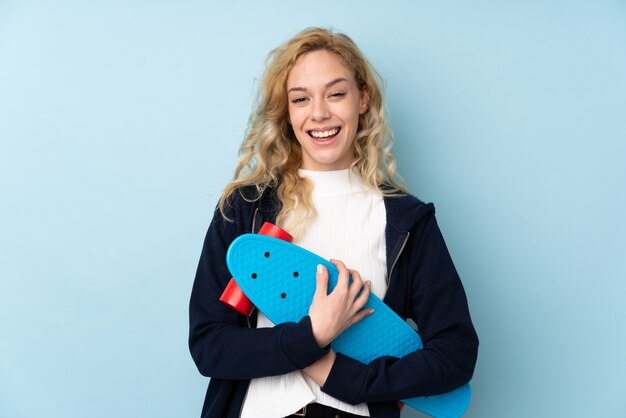 Jeune femme blonde isolée sur un mur bleu avec un patin avec une expression heureuse