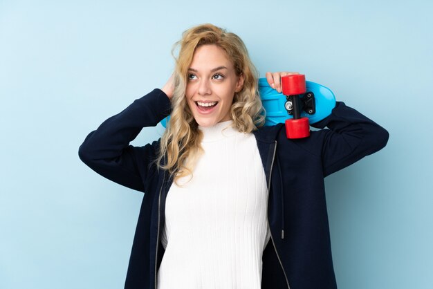 Jeune femme blonde isolée sur mur bleu avec un patin et levant