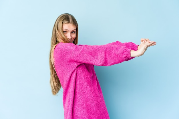 Jeune femme blonde isolée sur le mur bleu qui s'étend des bras, position détendue.