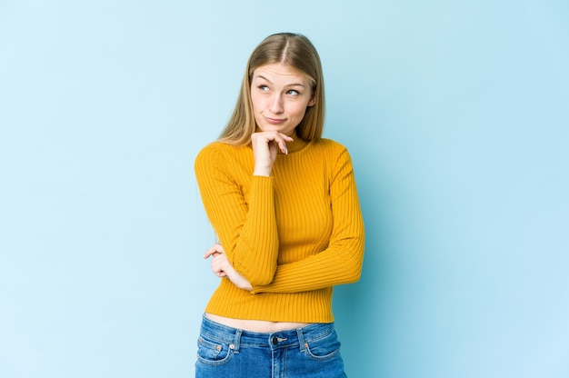 Jeune femme blonde isolée sur un mur bleu à la recherche de côté avec une expression douteuse et sceptique.