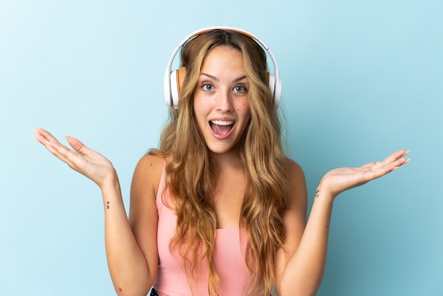 Jeune femme blonde isolée sur un mur bleu surpris et écouter de la musique