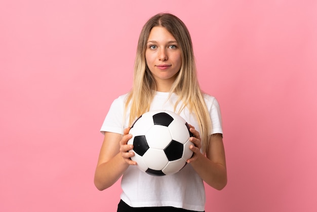 Jeune femme blonde isolée sur mur rose avec ballon de foot