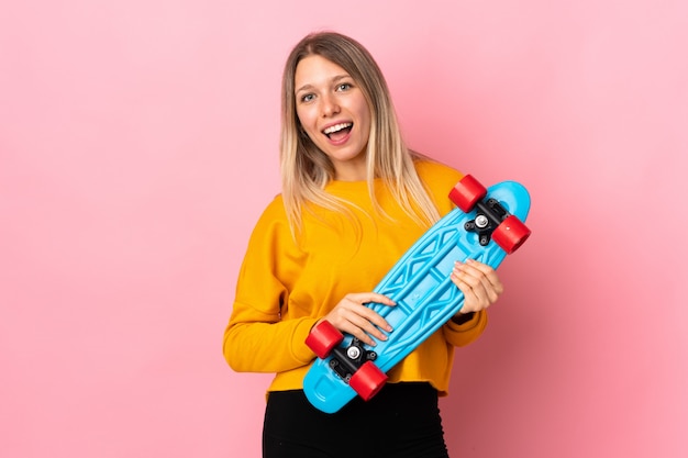 Jeune femme blonde isolée sur un mur rose avec un patin avec une expression heureuse