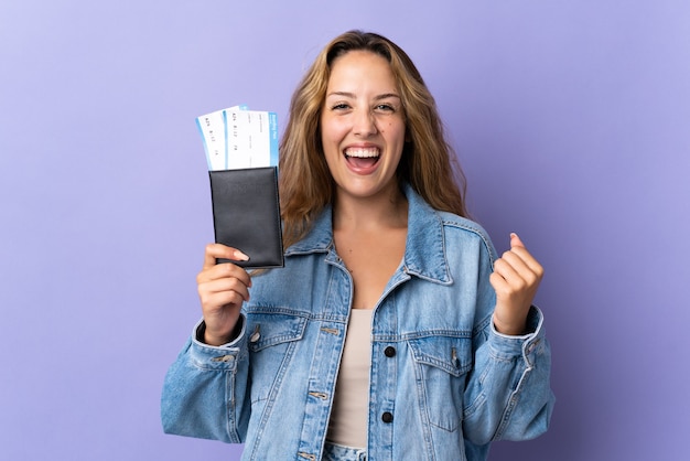 Jeune femme blonde isolée sur mur violet heureux en vacances avec passeport et billets d'avion