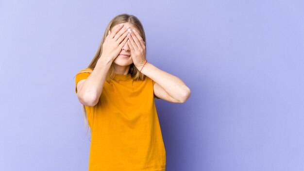 Jeune femme blonde isolée sur mur violet peur couvrant les yeux avec les mains